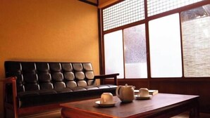A traditional Japanese room with tatami flooring, a black sofa, a wooden table with tea set, and a shoji screen window. - Higashi Matsuyacho West (Kyoto)