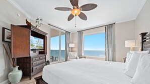Ein Hotelzimmer mit einem großen Bett, einem Deckenventilator, einem Fernseher, einem Schminktisch und Blick aufs Meer.