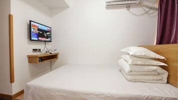 Une chambre d’hôtel avec un lit, un téléviseur posé sur un meuble, un appareil de climatisation et une étagère en bois.
