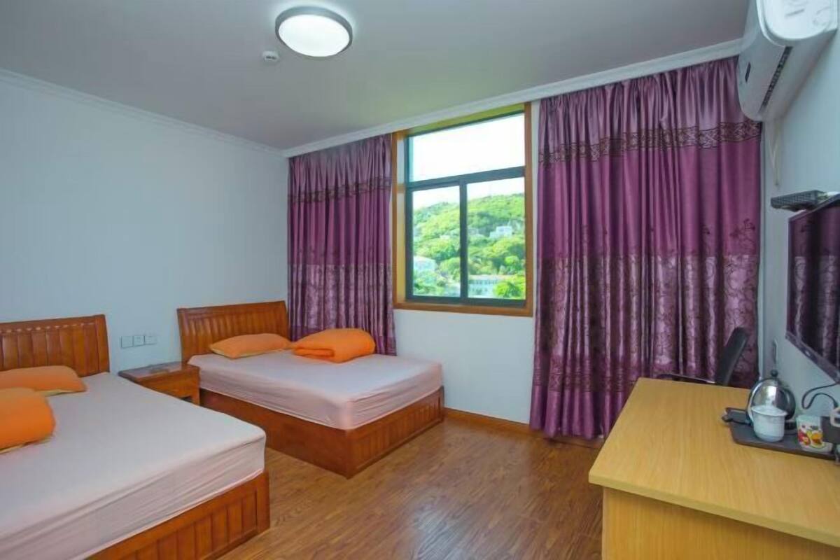 Ein Zimmer mit zwei Betten, einem Schreibtisch und einem Fenster mit Vorhängen.