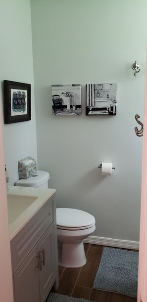 Een badkamer met een toilet, een wastafel en een kastje. Drie ingekaderde foto’s hangen aan de muur.