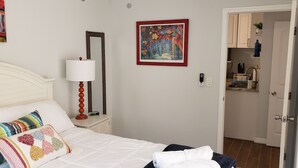 Un dormitorio con una cama, una mesita de noche con lámpara, un espejo y un cuadro en la pared.