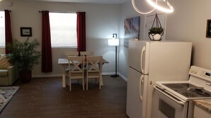 Cocina compacta con refrigerador, estufa y comedor con sillas y una mesa.