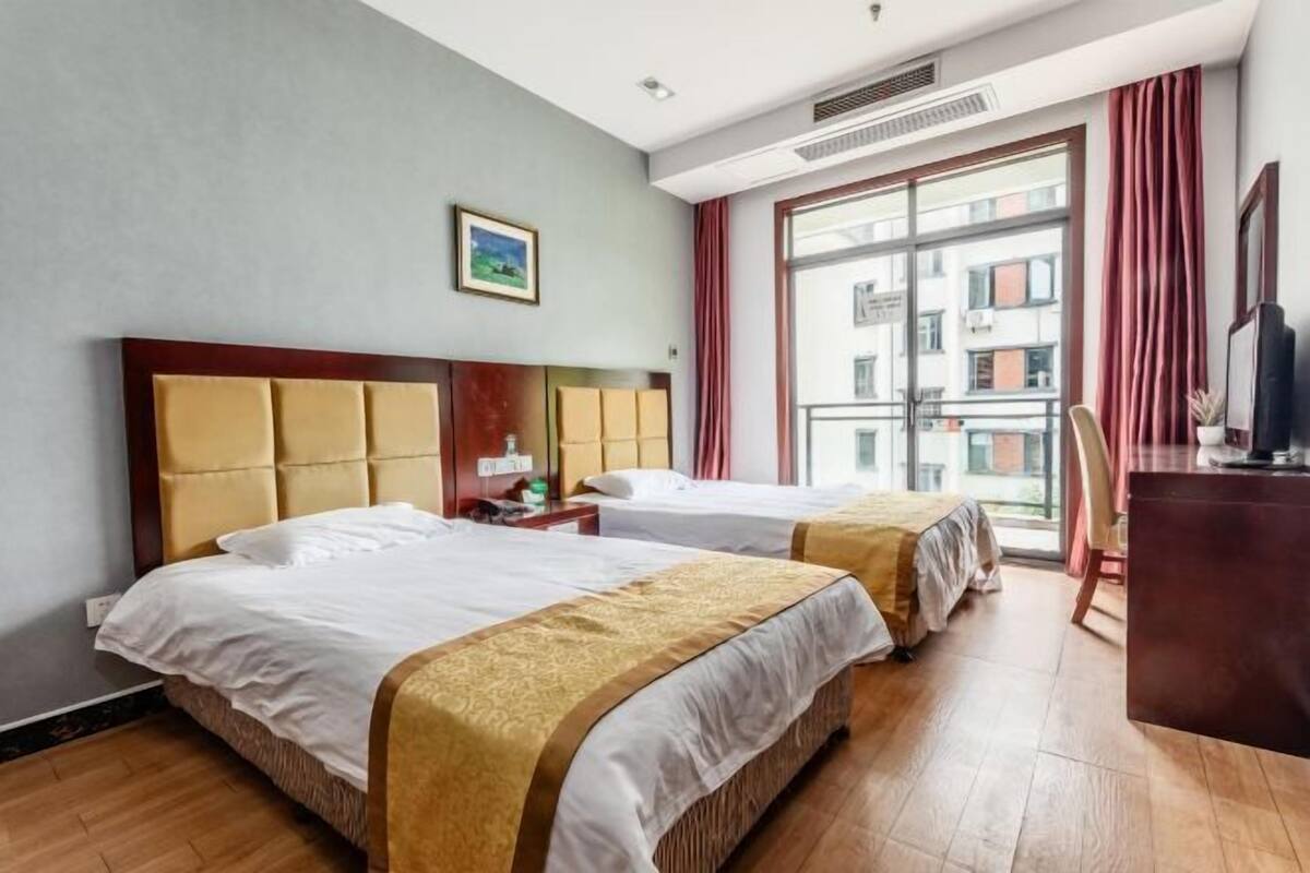 Hotellihuone, jossa on kaksi sänkyä, työpöytä, tuoli ja suuri ikkuna.