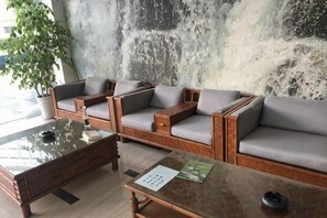 A seating area with sofas and a coffee table, a plant, and a textured wall. - Xinyu Holiday Hotel (Huangshan Tunxi) (Huangshan City)