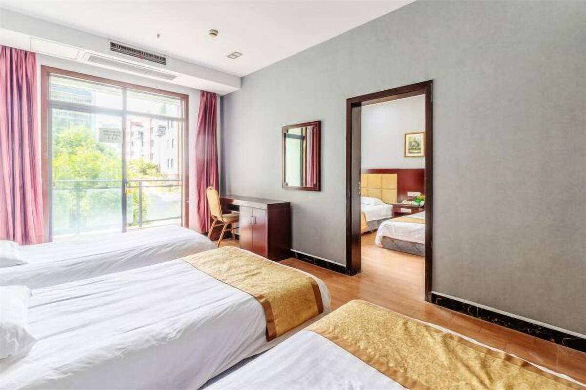 Hotellihuone, jossa on kaksi sänkyä, työpöytä, tuoli, peili ja näkymä ulos.