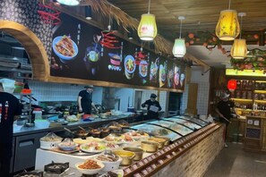 A restaurant with a variety of dishes displayed in the front, a bar area, and a kitchen in the background. - Xinyu Holiday Hotel (Huangshan Tunxi) (Huangshan City)