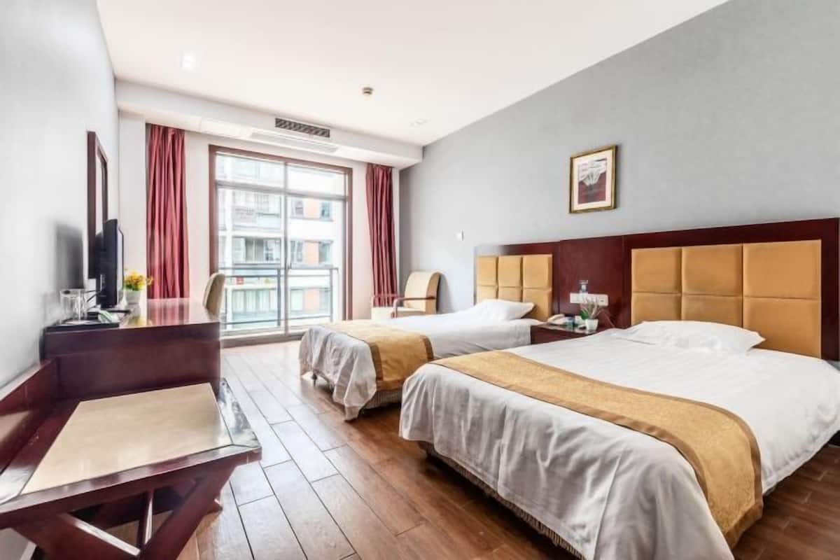 Hotellihuone, jossa on kaksi sänkyä, työpöytä, tuoli, televisio ja ikkuna, jossa on verhot.