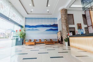 A hotel lobby with a reception desk, seating area, and a large wall mural. - Xinyu Holiday Hotel (Huangshan Tunxi) (Huangshan City)