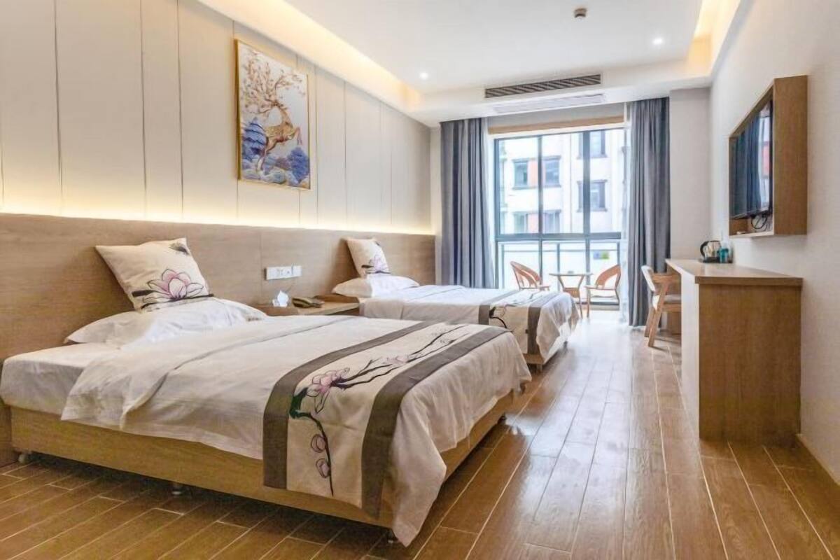 Hotellihuone, jossa on kaksi sänkyä, työpöytä, tuoli, televisio ja ikkuna, jossa on verhot.