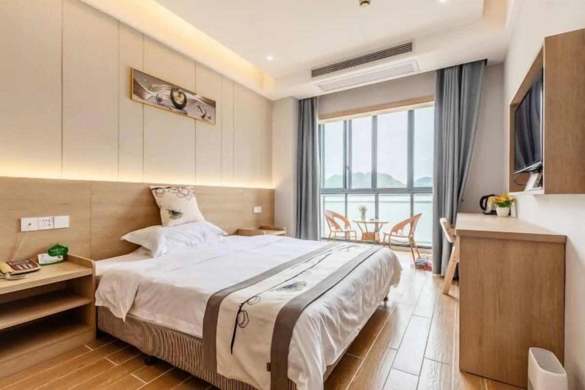 Moderni hotellihuone, jossa on suuri sänky, yöpöytä ja pieni työpiste.
