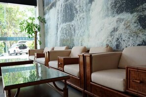 Uma área de estar com mesa de vidro e sofás, um mural grande na parede e vista para carros e vegetação lá fora.