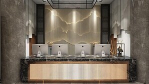 Een moderne receptiebalie met een marmeren aanrecht, meerdere Apple iMacs en een decoratieve wand met verticale lijnen.