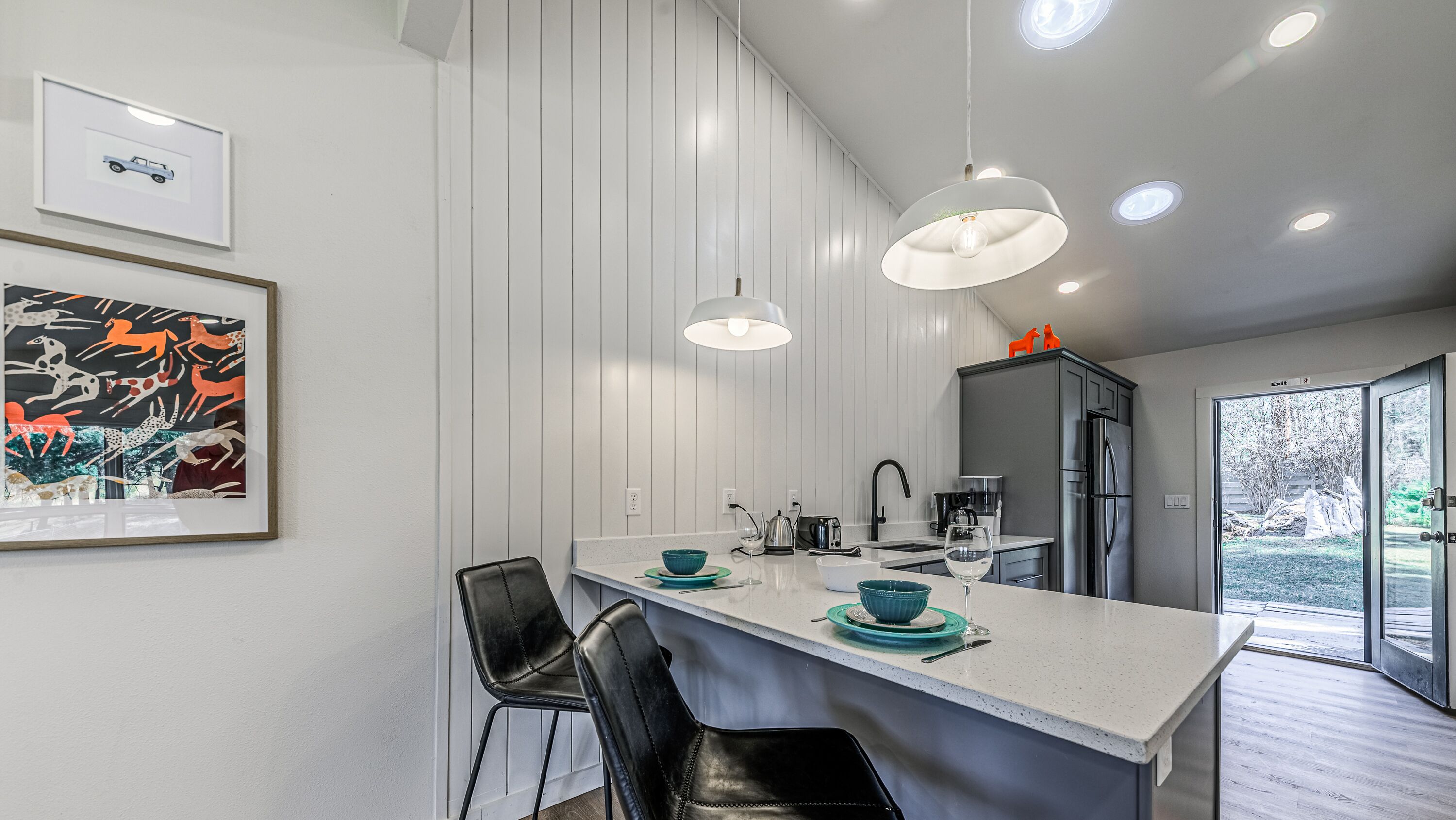 Une cuisine moderne dotée d’un îlot central, de tabourets de bar, de luminaires suspendus et offrant une vue sur l’extérieur.