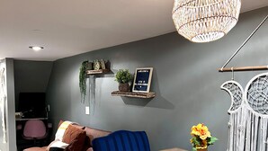 Una sala de estar moderna con sofá, sillones, una mesa de comedor y elementos decorativos como una lámpara colgante y cuadros en la pared.