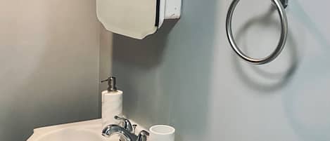 A bathroom with a white sink, a mirror, a towel ring, and a toilet paper holder.