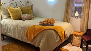 Un dormitorio ordenado con cama, lámpara de noche, una silla y una ventana con cortinas.