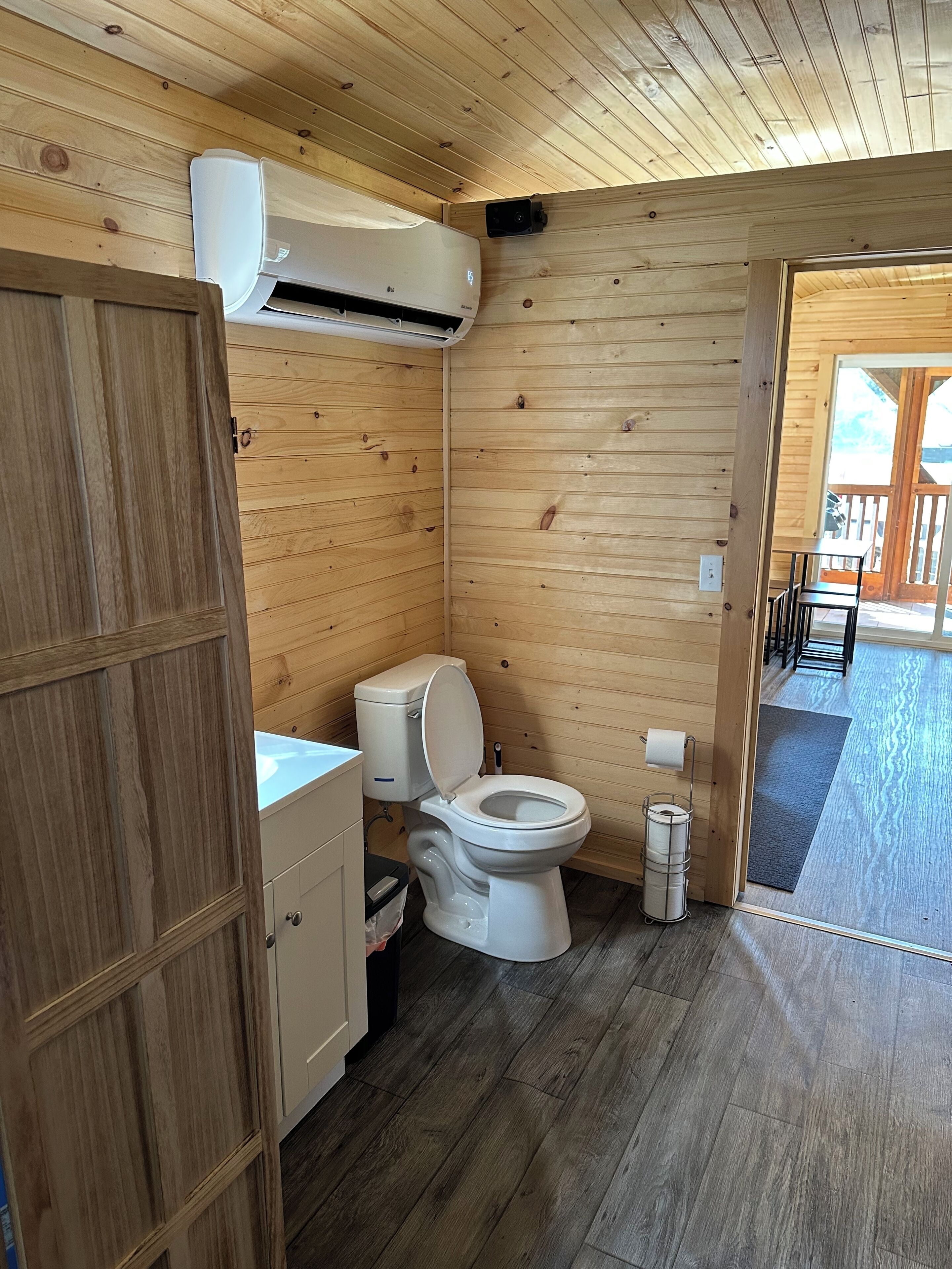 Un baño con paneles de madera, un inodoro, un mueble pequeño y un perchero para toallas.