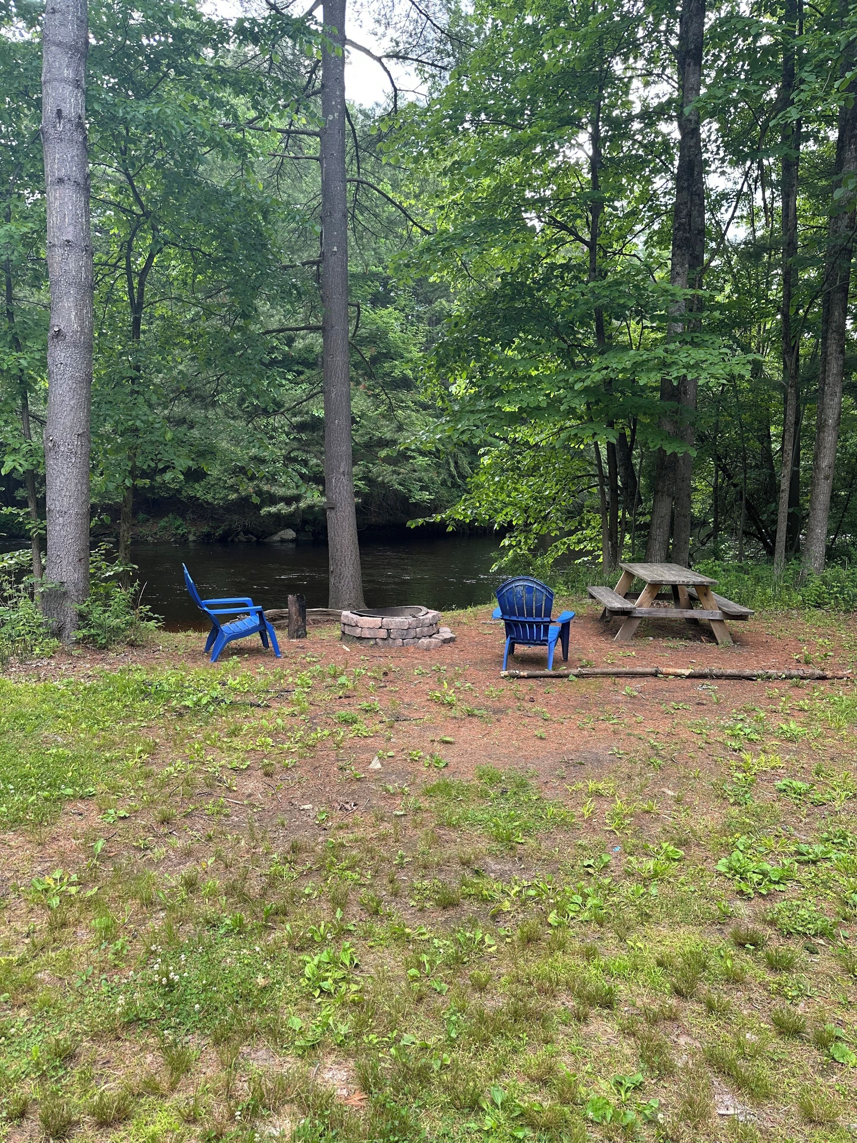 Un terrain de camping avec deux chaises bleues, un foyer et une table de pique-nique.