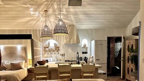 A modern living room with a sofa, a coffee table, and pendant lights. There is a kitchen area with a dining table and chairs visible in the background. - Ojai Serenity Retreat - Tranquil Valley Escape (Ojai)