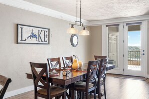 A dining area with a wooden table, chairs, a chandelier, a wall-mounted mirror, and a door leading to a balcony.