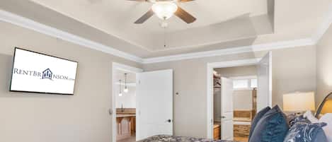 A bedroom with a bed, a ceiling fan, a bathroom visible through an open door, and a sign on the wall.