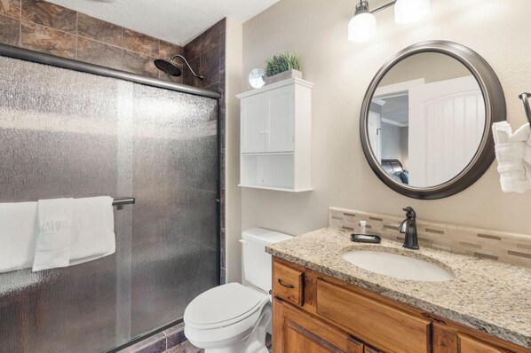 A modern bathroom with a glass-enclosed shower, a toilet, a sink with a vanity, and a mirror.