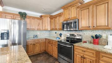 A kitchen with wooden cabinets, stainless steel appliances, granite countertops, and a tiled backsplash.