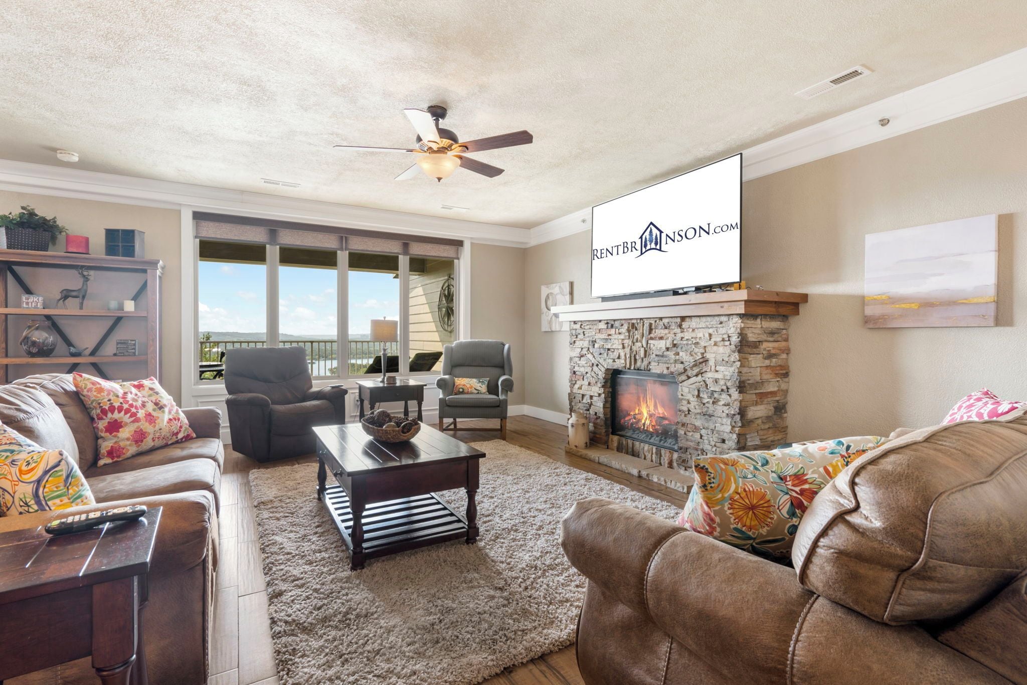 A living room with a fireplace, a ceiling fan, and a large window.