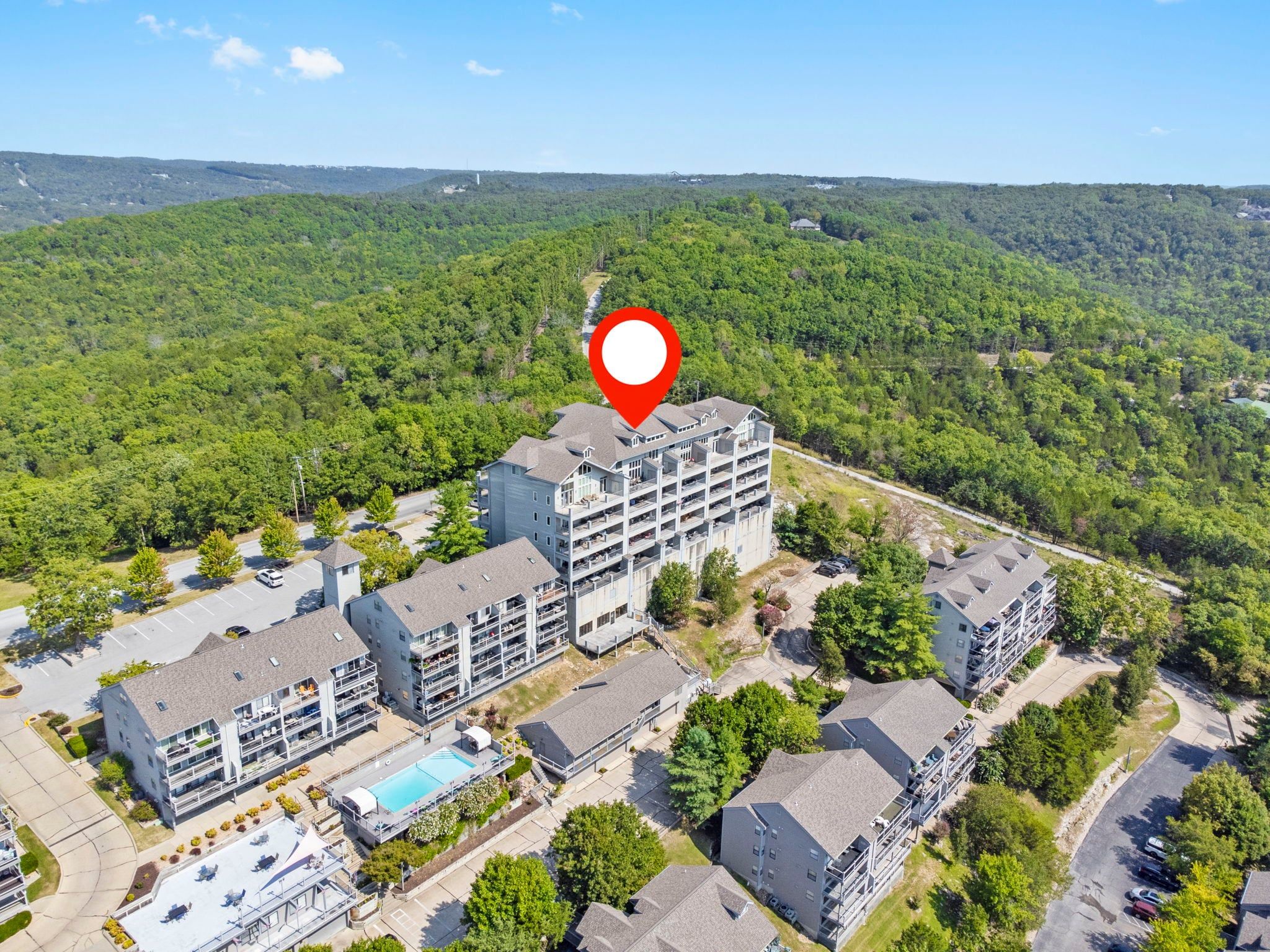 Um hotel com vários andares, piscina no terraço, cercado por vegetação exuberante e relevo montanhoso.