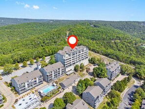 A multi-story hotel with a rooftop pool, surrounded by lush greenery and hilly terrain.