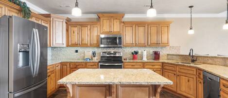 Cocina con armarios de madera, electrodomésticos de acero inoxidable, encimeras de granito e iluminación colgante.