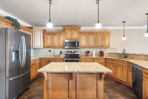 A kitchen with wooden cabinets, stainless steel appliances, granite countertops, and pendant lighting.