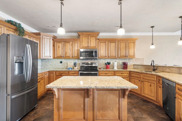 A kitchen with wooden cabinets, stainless steel appliances, granite countertops, and pendant lighting.
