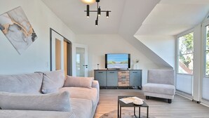 Een moderne woonkamer met een bank, fauteuil en een televisie op een houten kast.