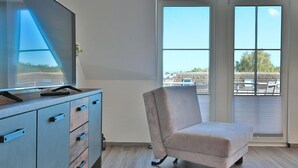 Een moderne kamer met een groot raam, een bureau met lades en een comfortabele fauteuil.