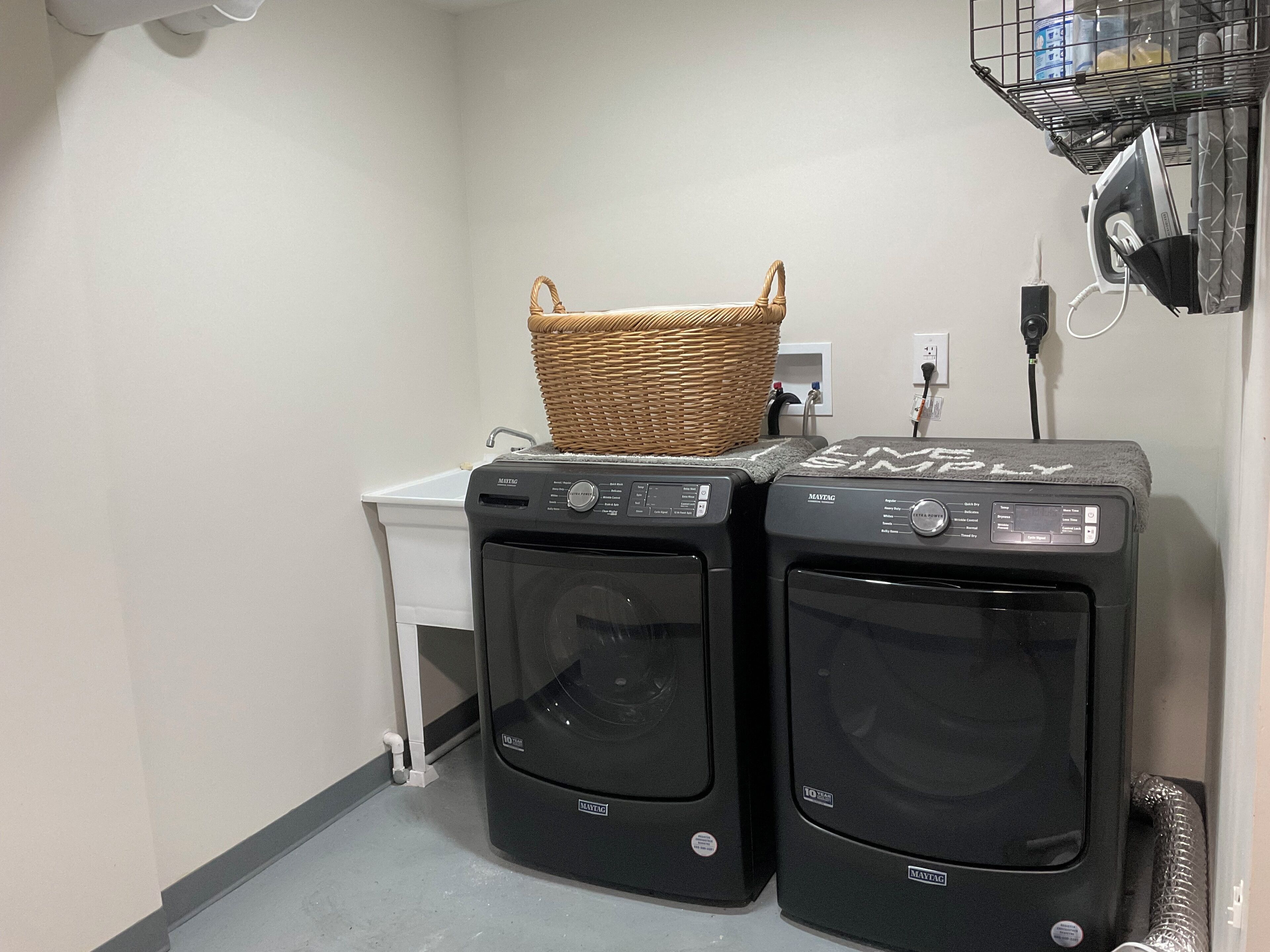 A laundry area with two Maytag front-loading washing machines, a small white laundry cart, and a wicker basket on top of the right machine.