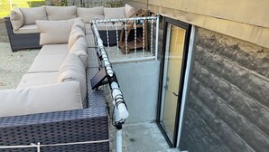 Un espace patio aménagé avec un canapé en osier, un hamac et une porte-fenêtre coulissante donnant sur un espace extérieur abrité.