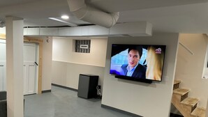 Un salon moderne avec un téléviseur à écran plat fixé au mur, un canapé gris et un escalier en bois.