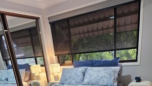 Un dormitorio con una cama grande, dos mesitas de noche, un espejo y una ventana con vistas a zonas verdes.