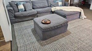 Un sofá seccional gris con un reposapiés a juego, una alfombra estampada y una taza blanca sobre el reposapiés.
