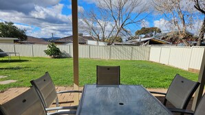 Un patio con mesa y sillas, un jardín cercado y vistas a casas al fondo.