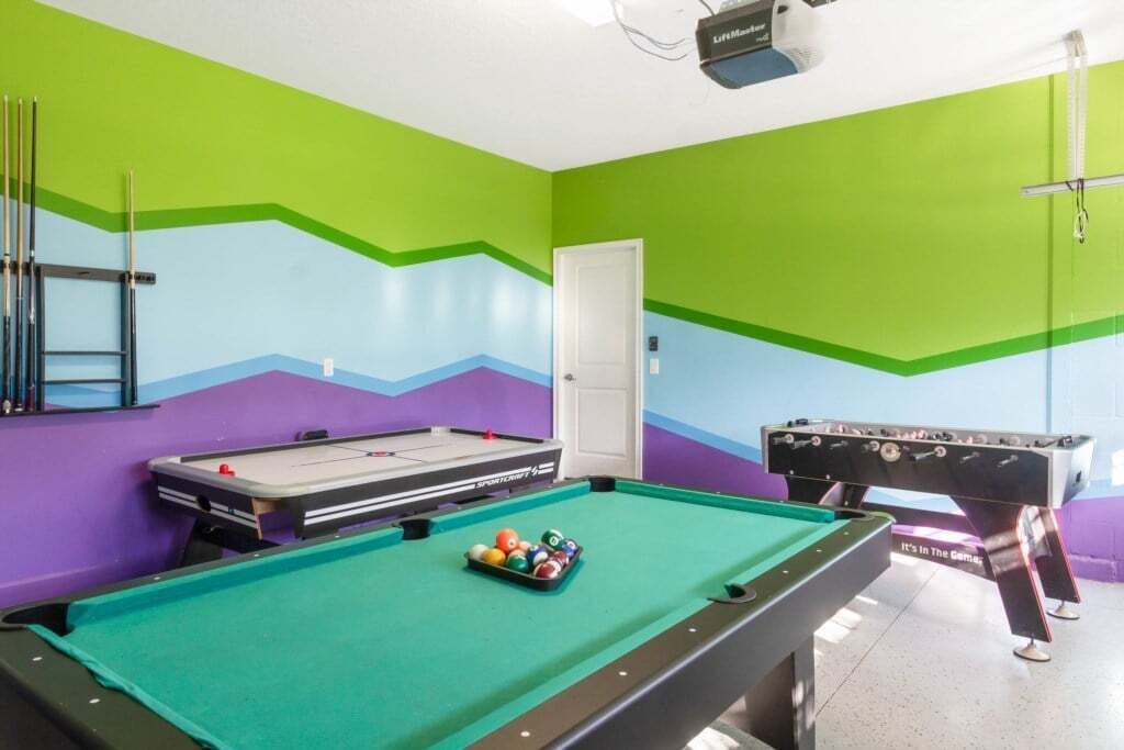 Une table de billard avec des billes, une table de baby-foot et un projecteur fixé au plafond.