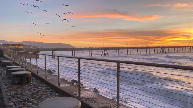 Un paseo marítimo con barandilla, piedras y vistas al mar durante el atardecer.