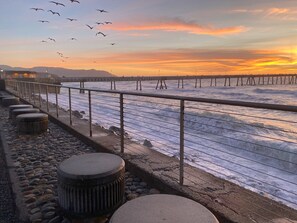 Een kustpad met een hekwerk, kiezels en een uitzicht op zee tijdens zonsondergang.