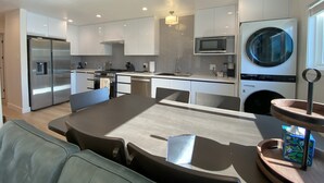 Una cocina moderna con armarios blancos, electrodomésticos de acero inoxidable y un comedor con mesa y sillas.