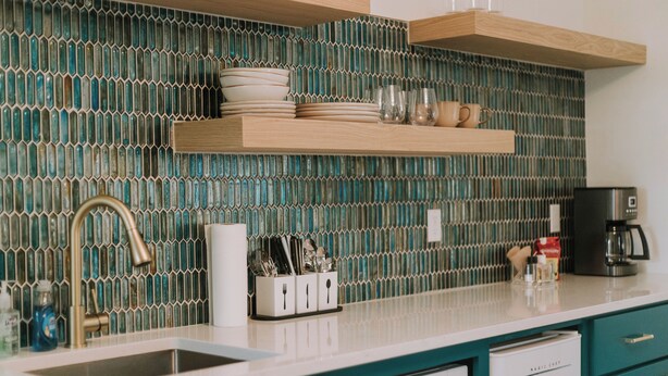 Une cuisine avec des meubles de couleur turquoise, un plan de travail blanc et un revêtement mural composé de carreaux verts et bleus.