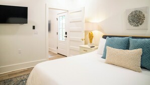 Une chambre d’hôtel comprenant un lit, un téléviseur fixé au mur, une table de chevet avec une lampe et une porte donnant sur une autre pièce.