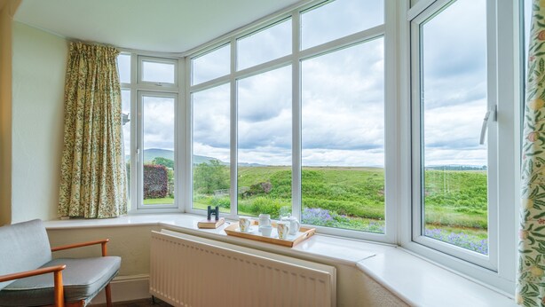 A room with a large bay window, a radiator, two wooden chairs, and a tray with tea set on the windowsill.