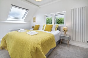 Een slaapkamer met een bed, twee ramen, een nachtkastje en een radiator.